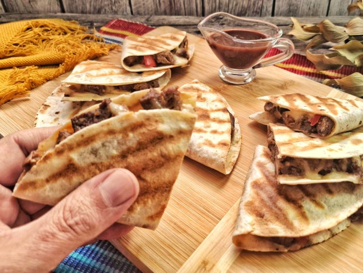 Quesadilla de carne finalizada com uma mão segurando um pedaço.