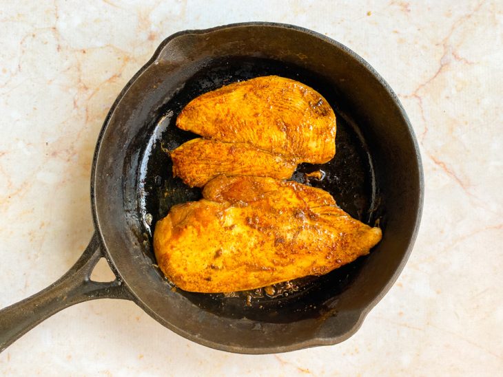 Filés de frango dourando em uma frigideira com azeite.