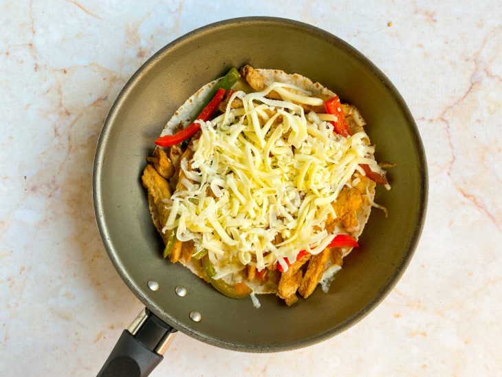 Frigideira com uma tortilha com o recheio de frango e queijo ralado por cima.