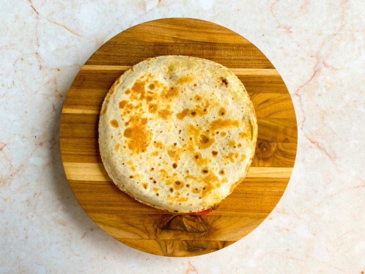 Tortilha recheada de frango e queijo coberta por outra tortilha em uma tabua de madeira.