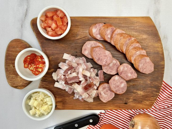 Uma tábua com linguiça calabresa, bacon, tomates, cebola e pimenta-de-cheiro picados.