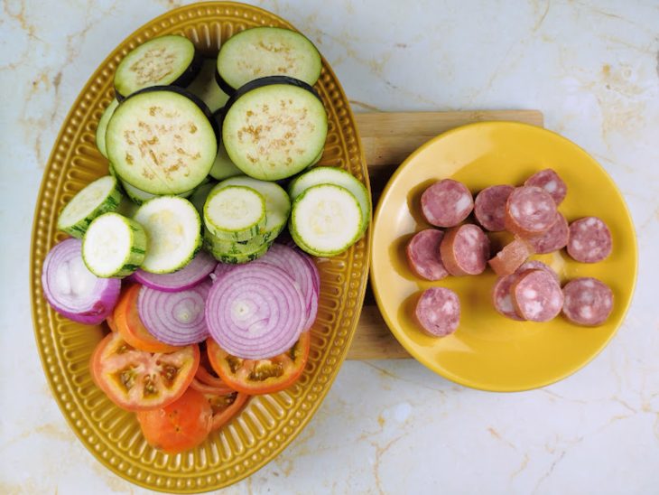 recipiente com linguiça calabresa, cebola, berinjela, abobrinha e tomate cortados em rodelas