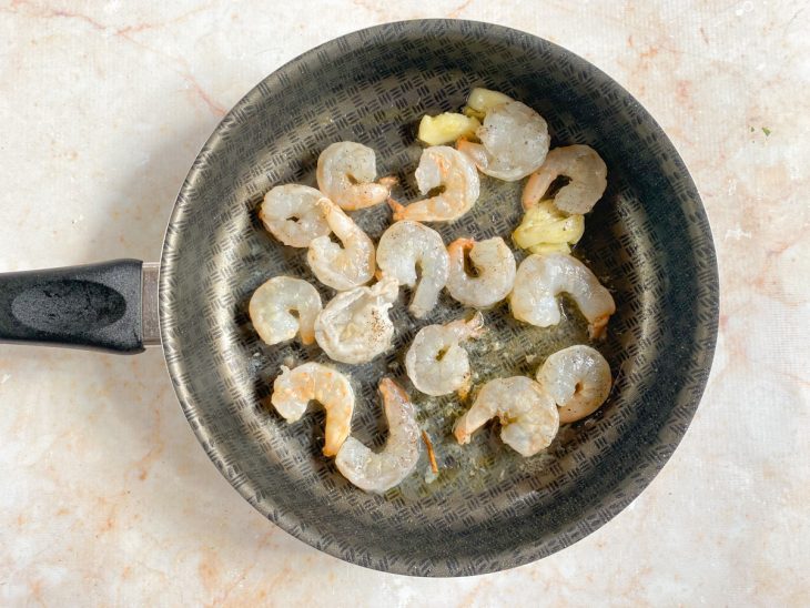 Porção de camarão com sal, pimenta-do-reino, alho espremido e azeite em uma panela.