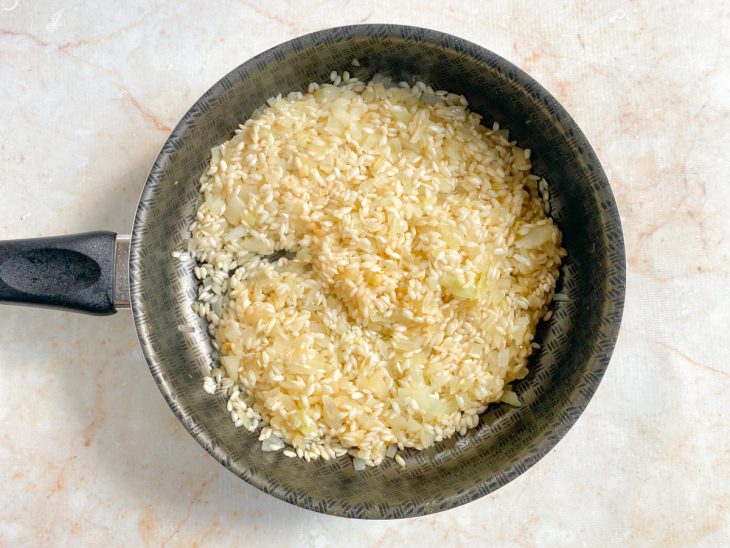 Porção de arroz arbóreo e vinho branco seco adicionados à panela.