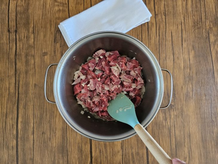 carne em uma panela junto com alho e cebola sendo mexida por uma espátula.