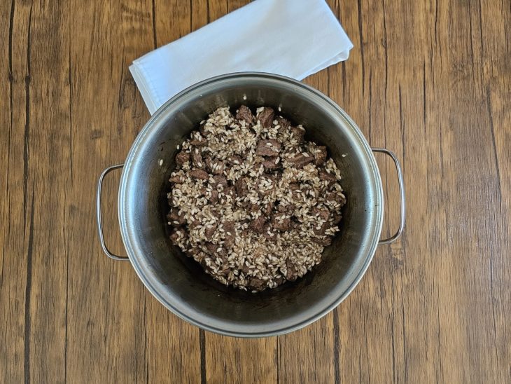 carne refogada com arroz ainda cru por cima em uma panela.