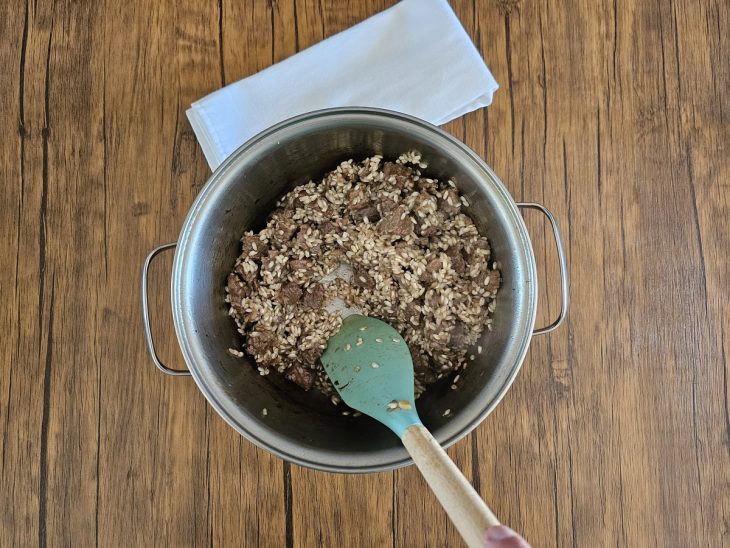 mistura de carne refogada com arroz e vinho branco sendo mexido por uma espátula.