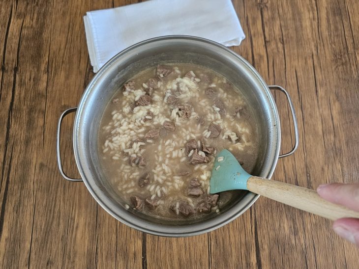 mistura do risoto submerso no caldo sendo mexido por uma espátula e queijo parmesão ralado adicionado a mistura.