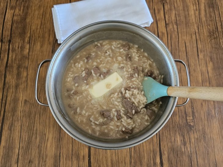 mistura do risoto com um pedaço de manteiga adicionado sendo mexido por uma espátula.