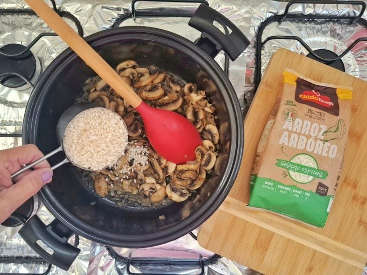 Cebola sendo refogada em uma panela com manteiga. Arroz arbóreo Caldo Bom sendo adicionado.