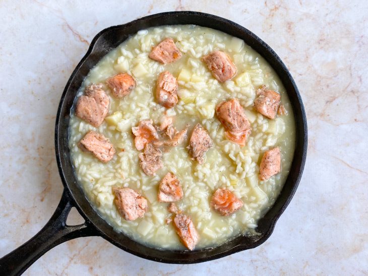 Uma frigideira com o arroz, o caldo, salmão e temperos.