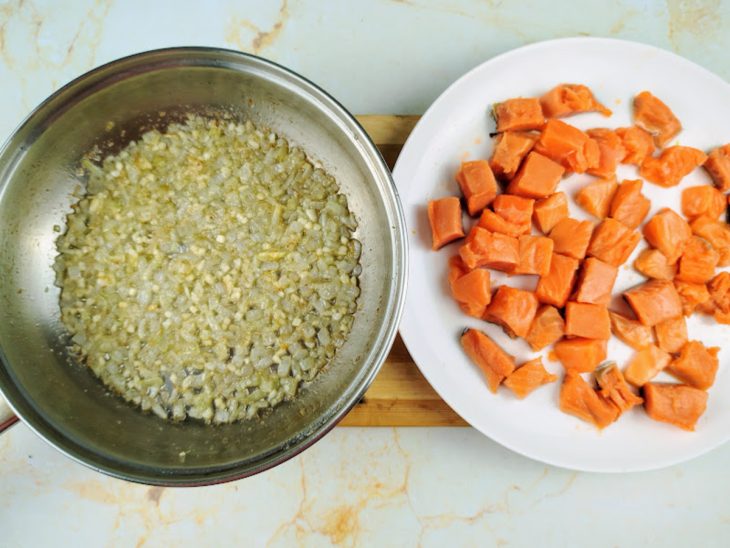 Um prato com salmão picado em cubos e uma panela com cebola e alho dourados.