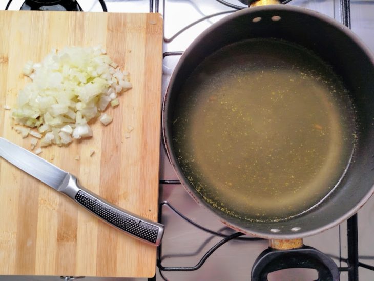 Cebola picada em uma tábua e panela com caldo de legumes.