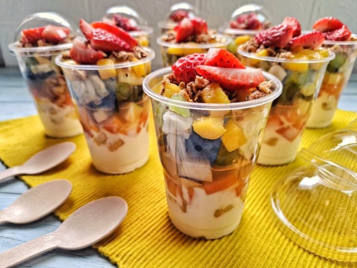 Uma bancada com saladas de frutas no pote com iogurte.