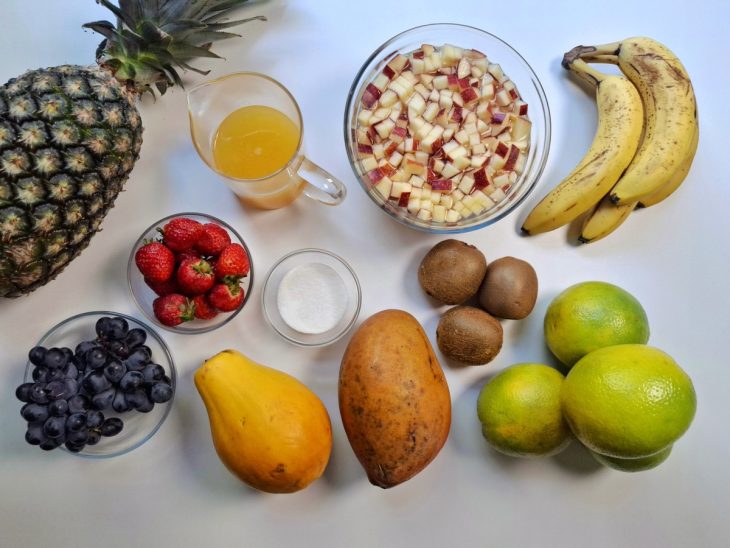 Ingredientes reunidos em uma bancada. Maçãs picadas em um recipiente com água e suco de limão.