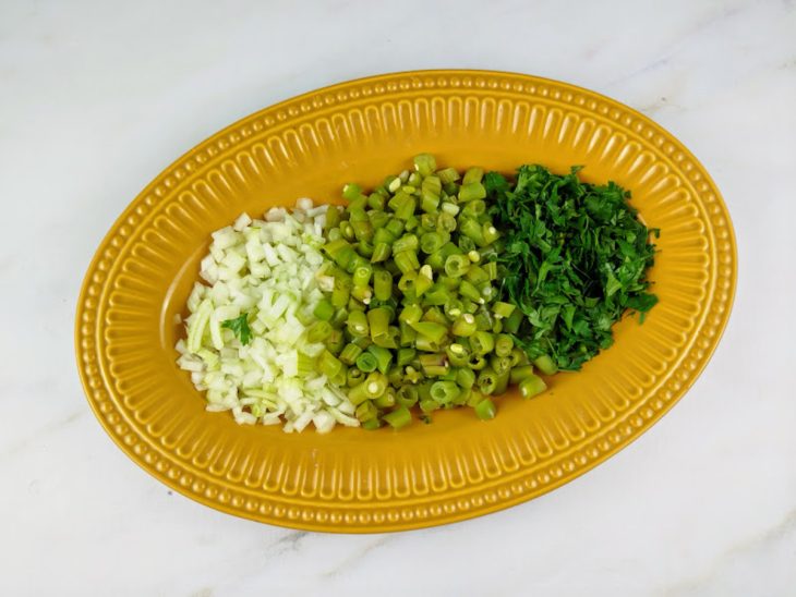 Vagem, cebola, salsinha e cebolinha picada em um prato.