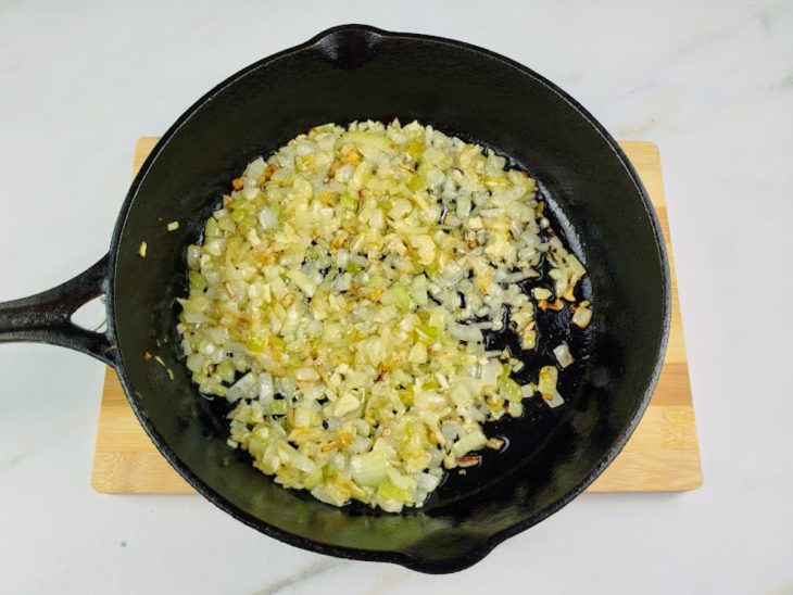 Uma frigideira com azeite, cebola e alho a refogar.