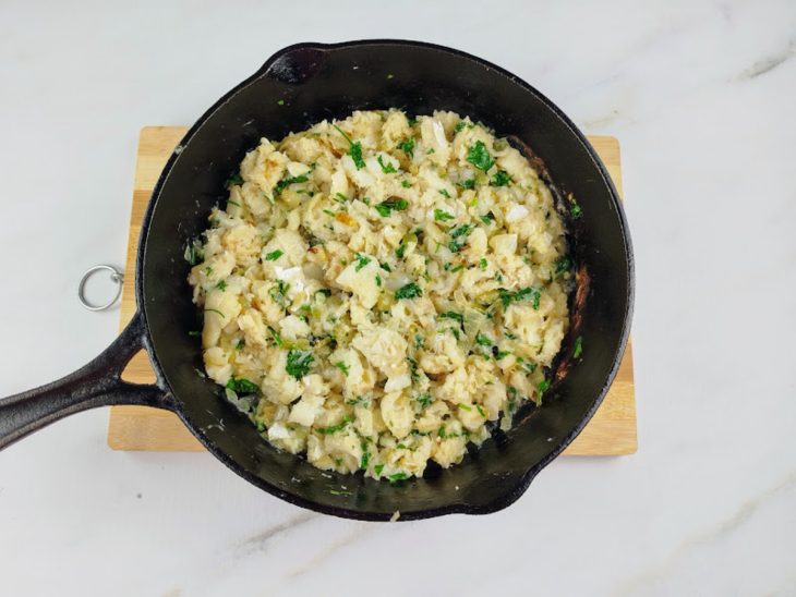 Uma frigideira com azeite, cebola, alho, bacalhau e salsinha.