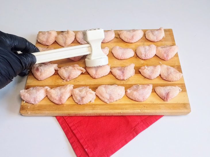 Uma tábua com sambiquiras de frango sendo amassadas.