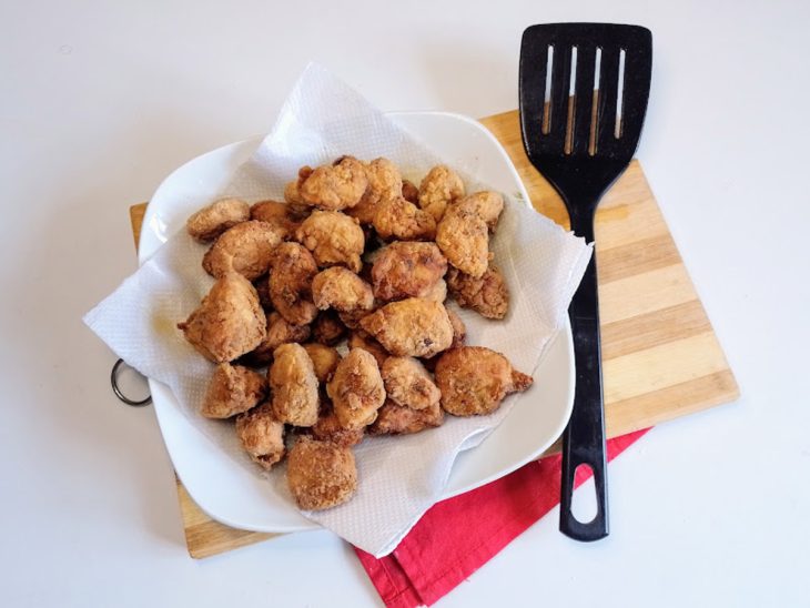 Uma escumadeira e um prato com papel-toalha contendo sambiquira de frango.