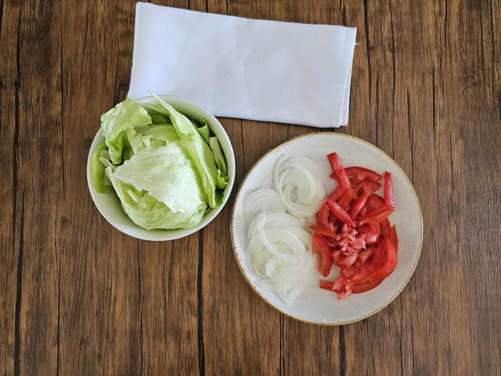 Pratos contendo alface, tomate e cebola fatiados.