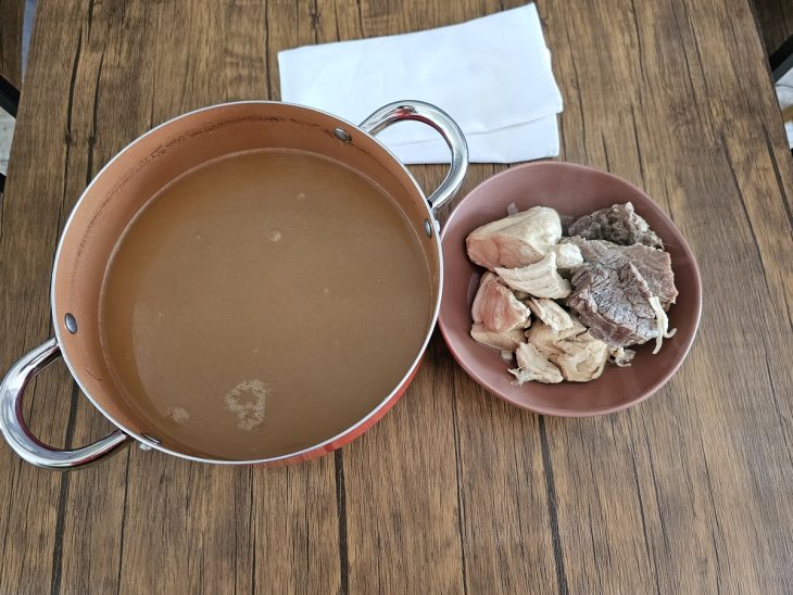 Uma panela com a água do cozimento e um prato com as carnes.