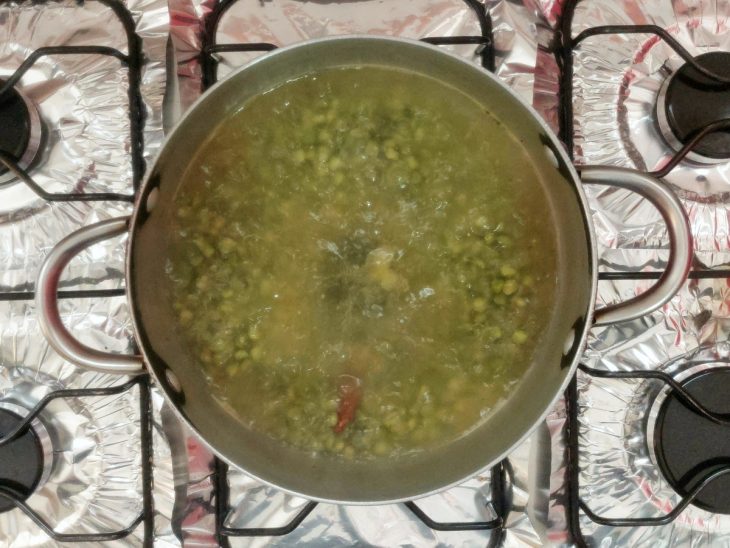 Uma panela com ervilhas, caldo de legumes, louro, sal e canela em processo de cozimento.