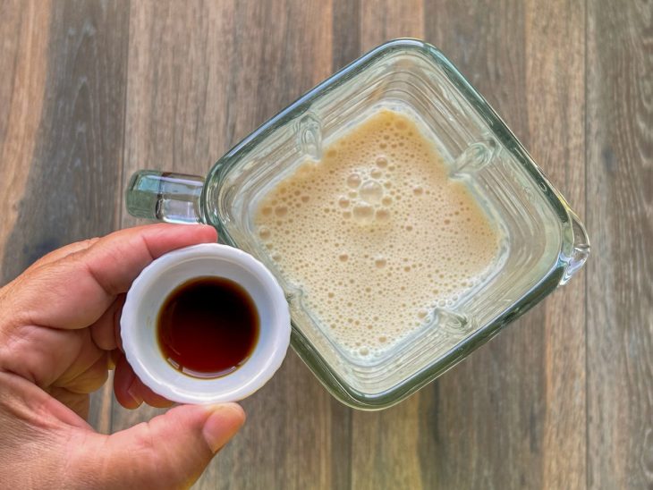 Creme de leite e leite condensado batidos no liquidificador e um pequeno pote com essência de baunilha que será adicionada.