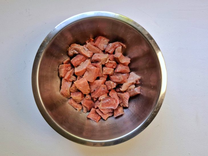 Carne picada em cubos acomodada em um recipiente e temperada com sal e pimenta-do-reino.