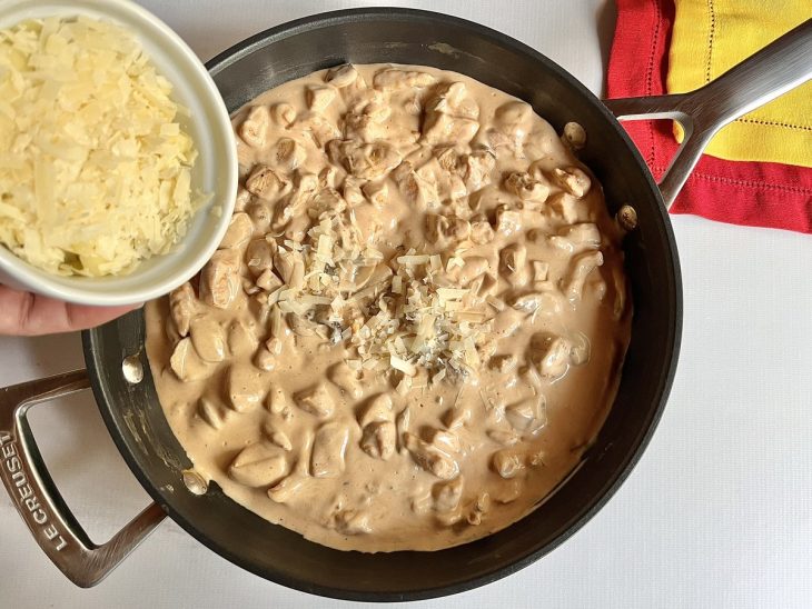 Uma panela com strogonoff e a adição de queijo e creme de leite.