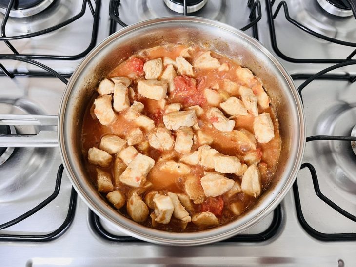 Uma panela com frango, cebola e tomate pelado.