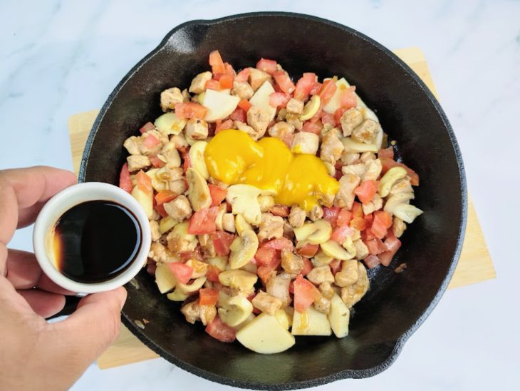 Uma frigideira refogando cebola picada, peito de frango cortado, tomate, champignon, mostarda, molho inglês e sal.