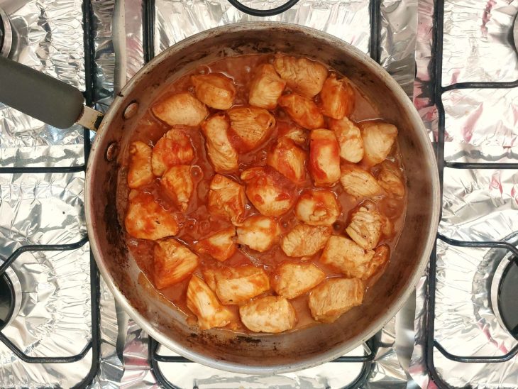 Uma panela com frango refogado, molho de tomate e temperos.