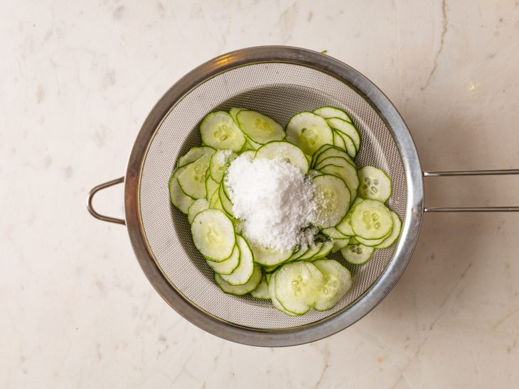 Fatias de pepino em uma peneira com sal por cima para desidratação.