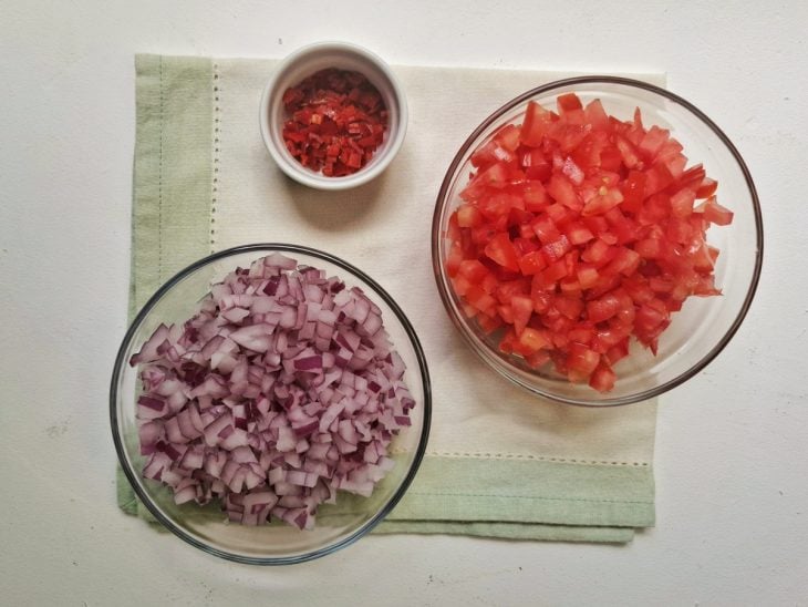 Recipientes com tomate, cebola e pimenta picados.