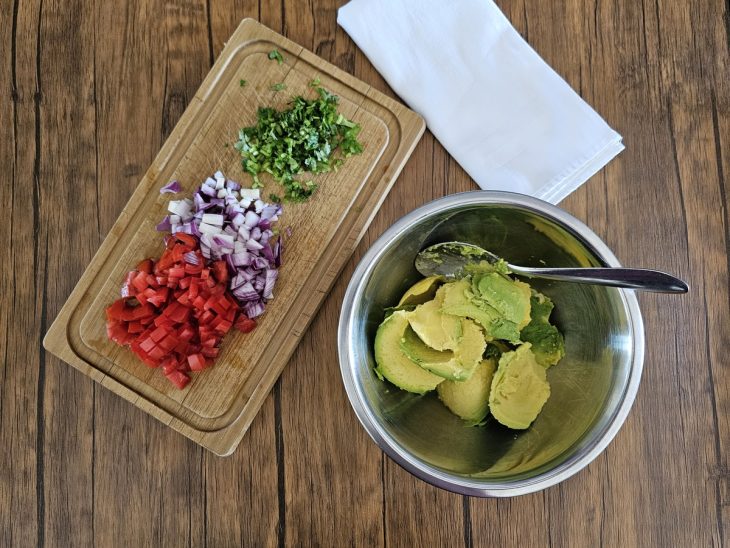 Uma tábua com cebola, tomate e coentro picados, e um recipiente com abacate.