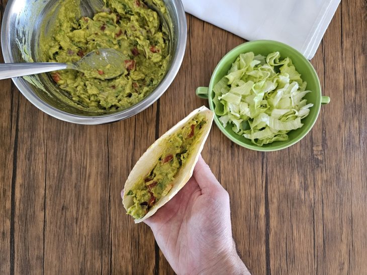 Um taco sendo recheado com guacamole e alface.