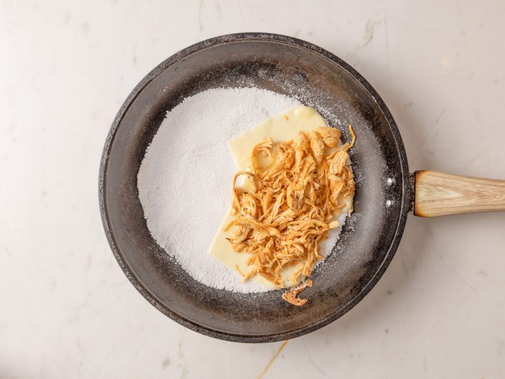 Queijo e frango desfiado adicionados sobre a tapioca.