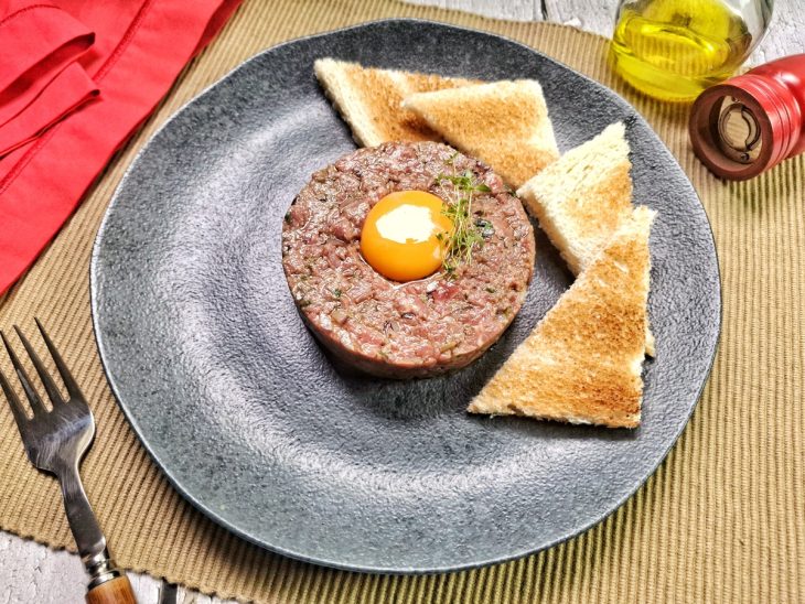 Tartar finalizado com uma gema de ovo ao centro e servido em um prato com torradas.