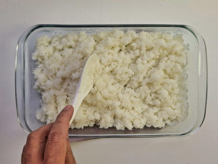 Arroz em travessa sendo temperado com molho su.