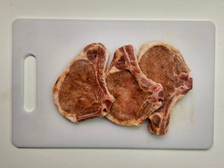 Uma tábua contendo filés de carne de porco sendo temperadas.