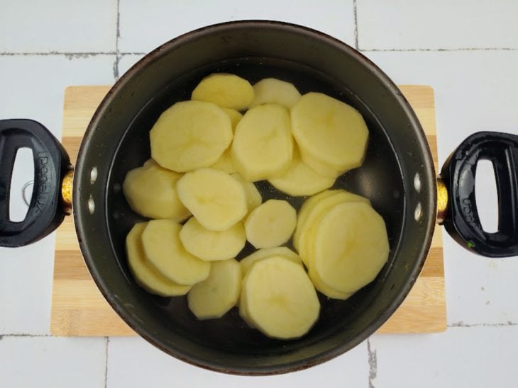 Batatas cortadas em rodelas em uma panela com água.