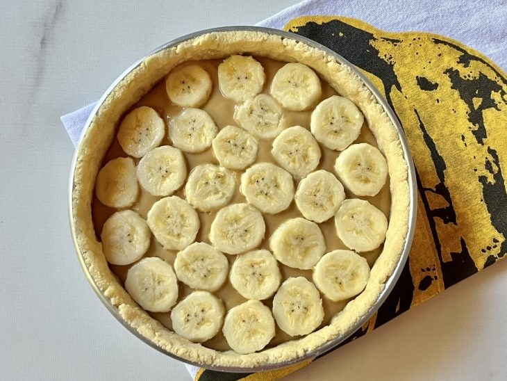 Uma forma contendo massa coberta com doce de leite e rodelas de banana.