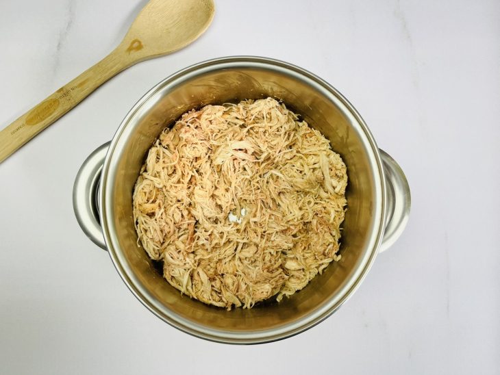 Alho, cebola, polpa de tomate e frango desfiado em uma panela.