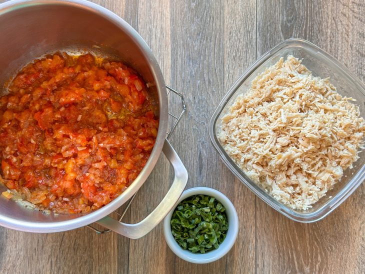 Frango desfiado e cebolinha para refogar na panela com tomates.