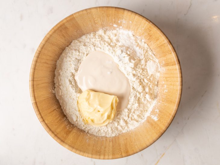 Farinha de trigo com manteiga, creme de leite e fermento em pó em uma tigela.