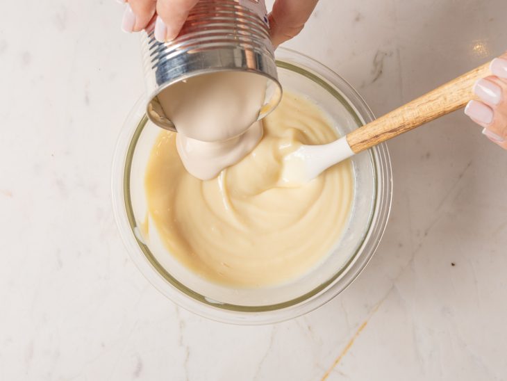 Creme de leite sendo adicionado em um pote de vidro com leite condensado e suco de limão para fazer o recheio.