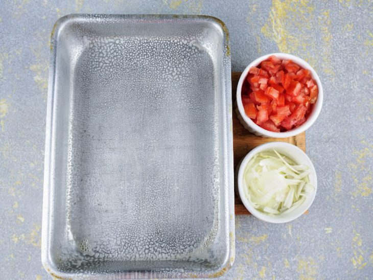 Tomate e cebola picados em recipientes, e forma retangular untada.