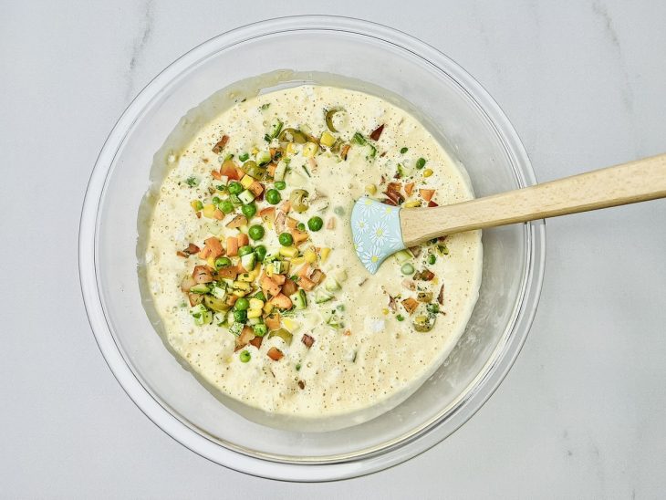 Massa despejada em uma tigela com fermento e legumes incorporados.