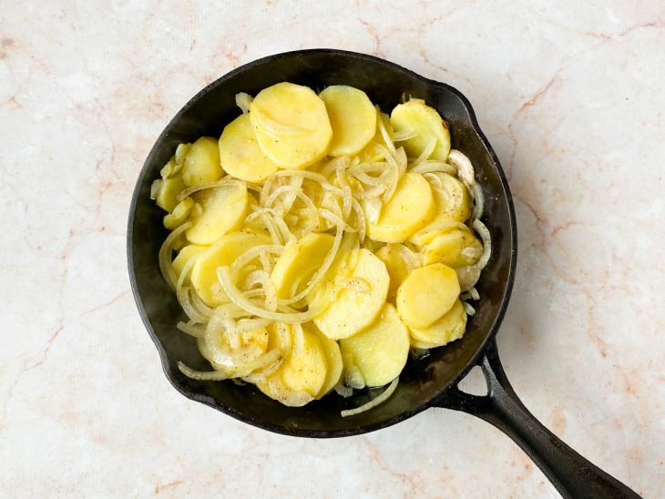 Batatas, cebolas, azeite e temperos na frigideira.